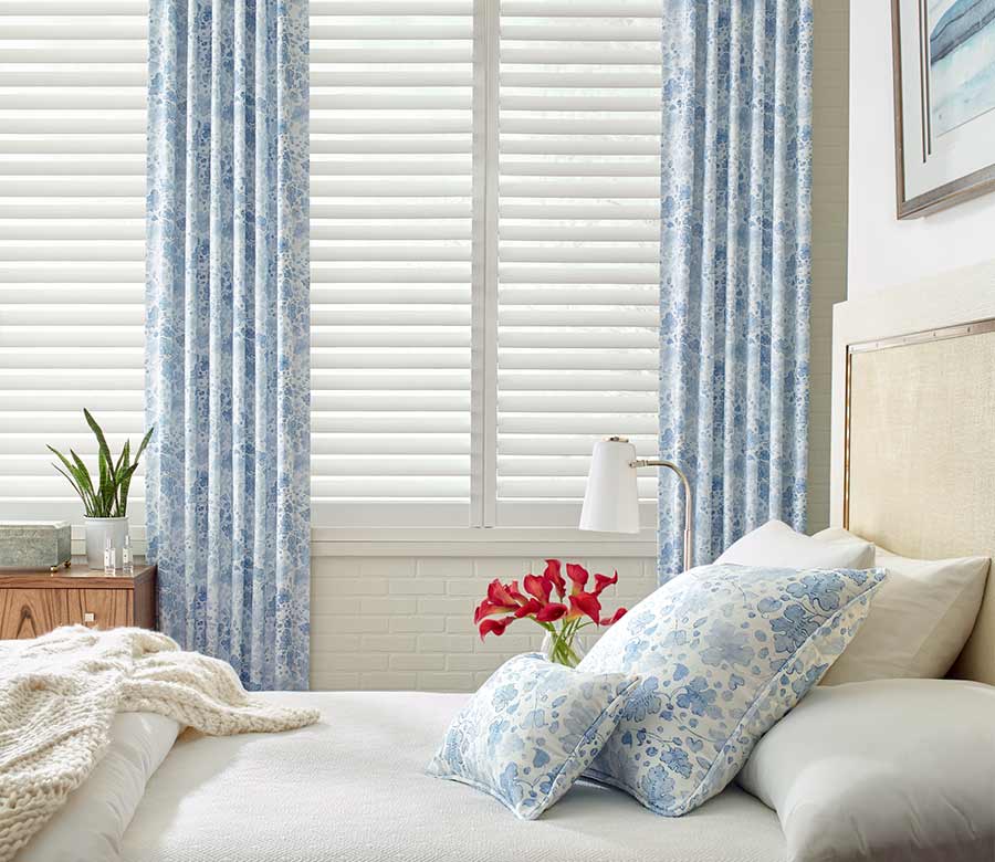 coastal guest bedroom white plantation shutters framed by blue floral curtains in naples, fl