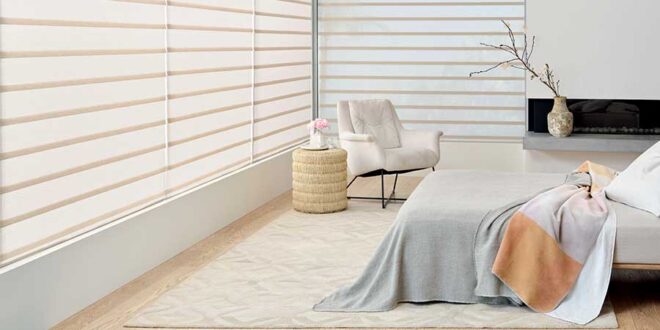 A white bedroom with rolling roman shades on the windows.
