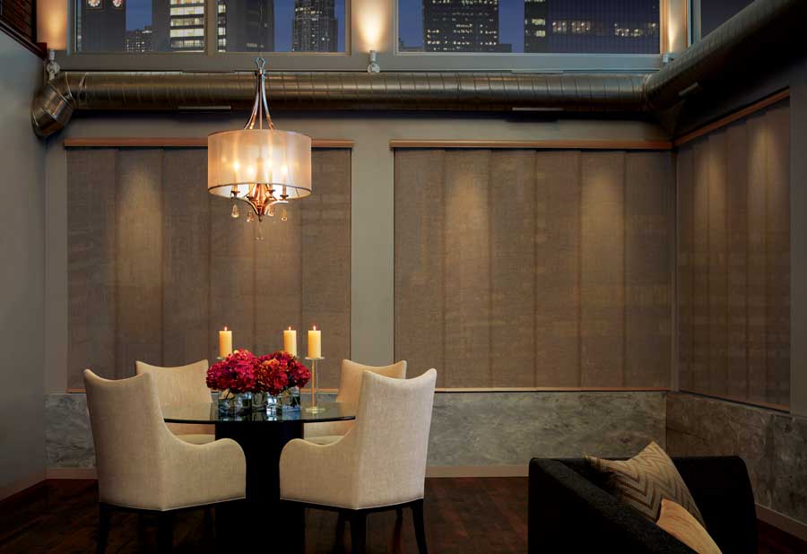 Cozy dining room with four cloth chairs, closed window panels and a chandelier providing soft lighting