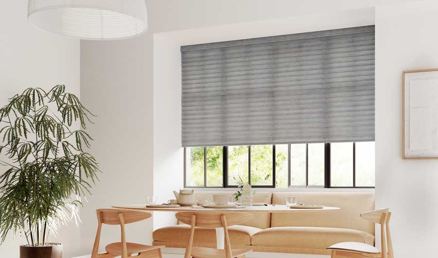 A light colored eat in dining space with gray cellular roller shades rolled halfway down the window.