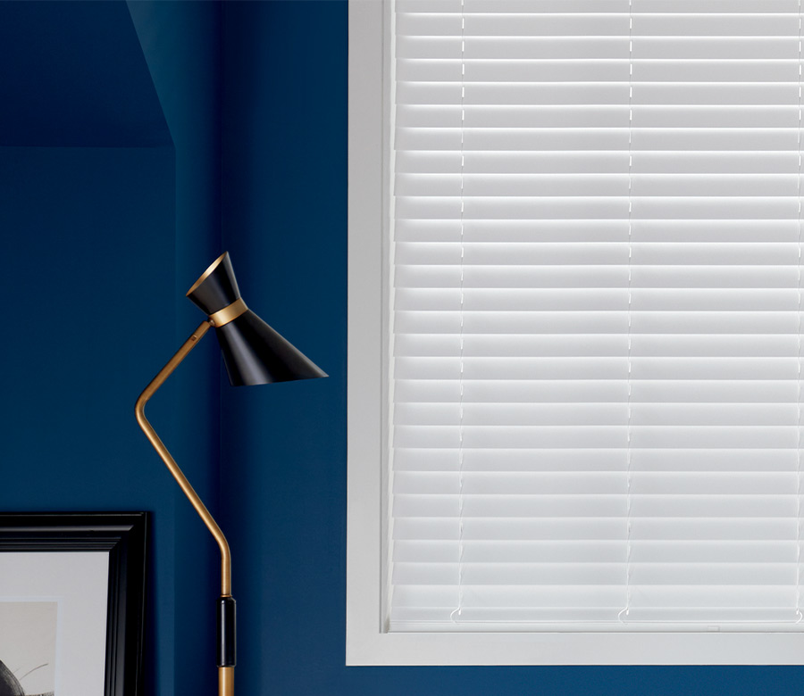 white composite blinds next to white fabric chair and modern lamp