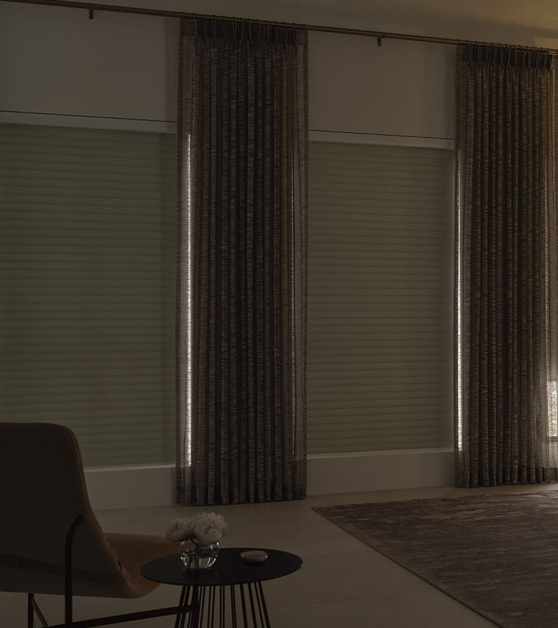 living room windows with neutral colored window shades with drapery in living room